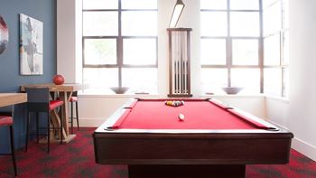 A pool table with a red cloth and white balls is in the center of the room at Skye at Belltown Apartments, Seattle, WA